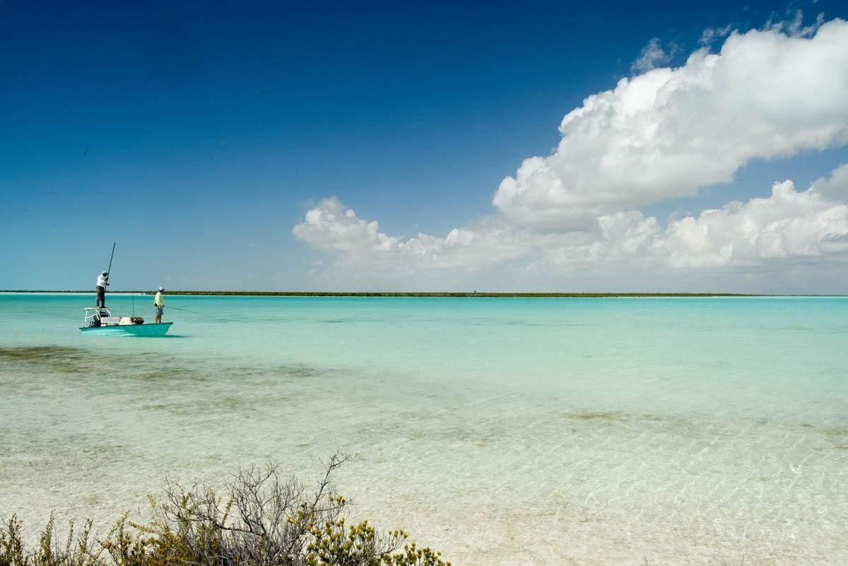Turquoise beach with a small boat on calm water under a bright blue sky with clouds