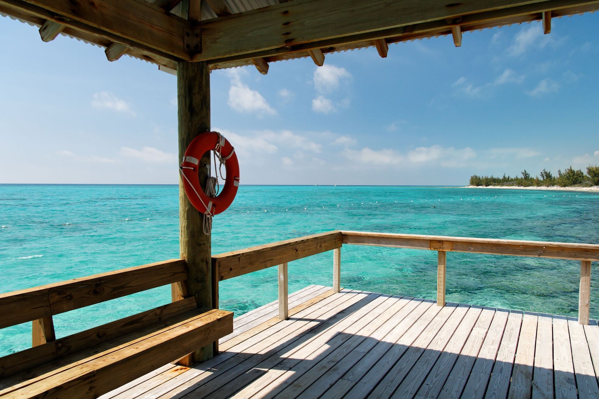 Wooden seaside deck with a red lifebuoy, overlooking turquoise water and a distant shoreline