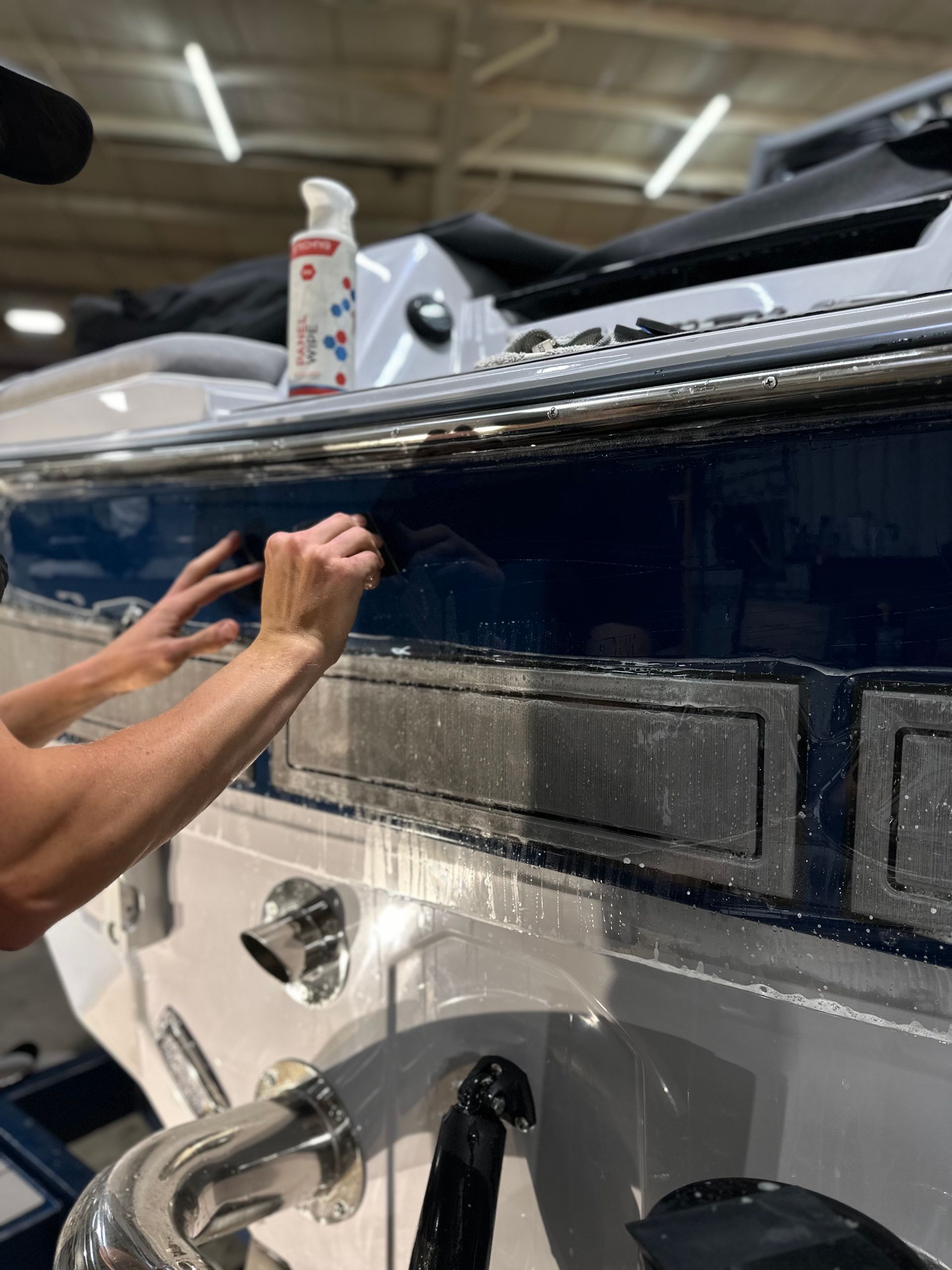Person cleaning a blue boat with a spray bottle, outdoors.
