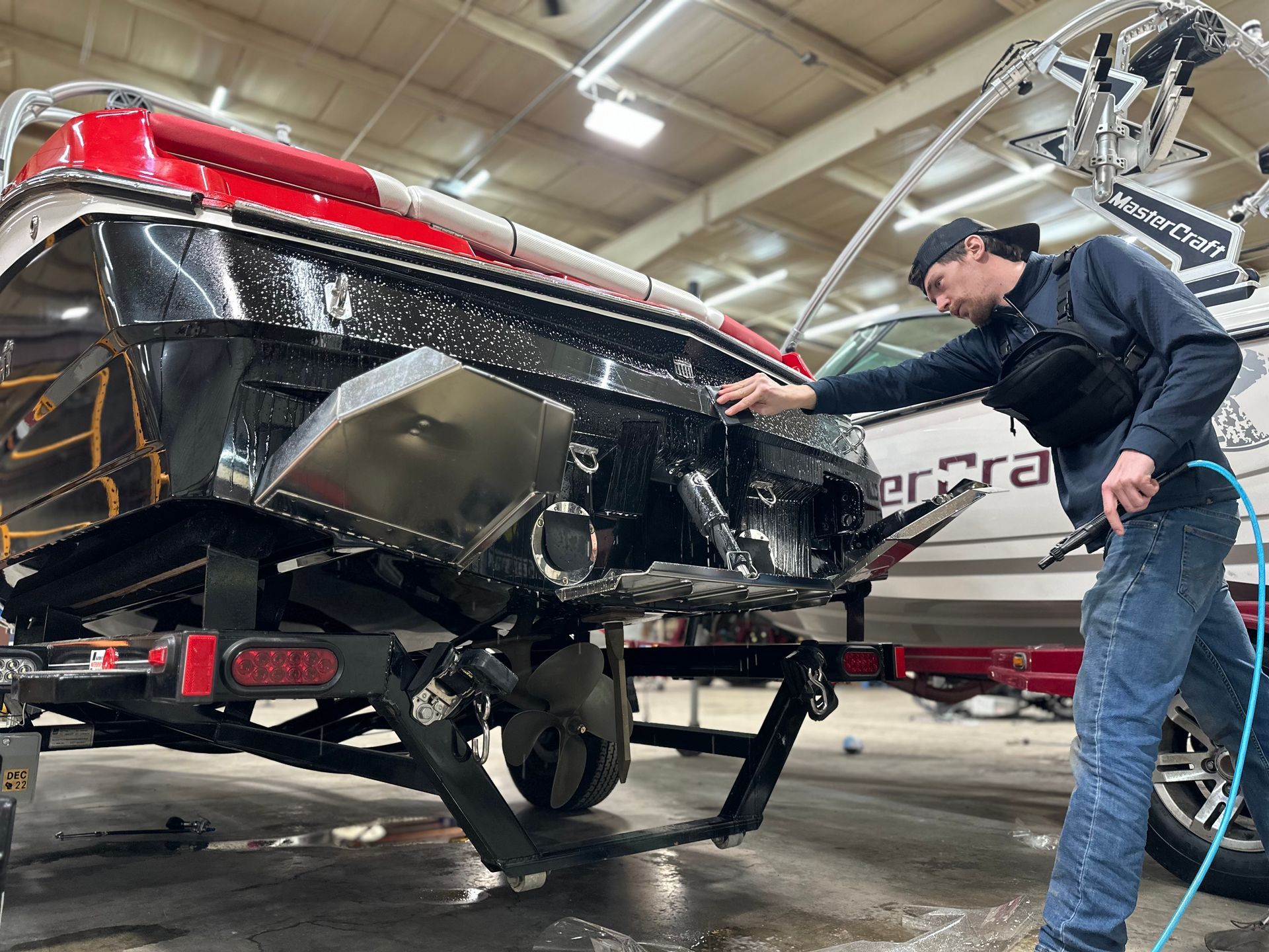 Man cleaning a black and red boat with a pressure washer inside a garage.