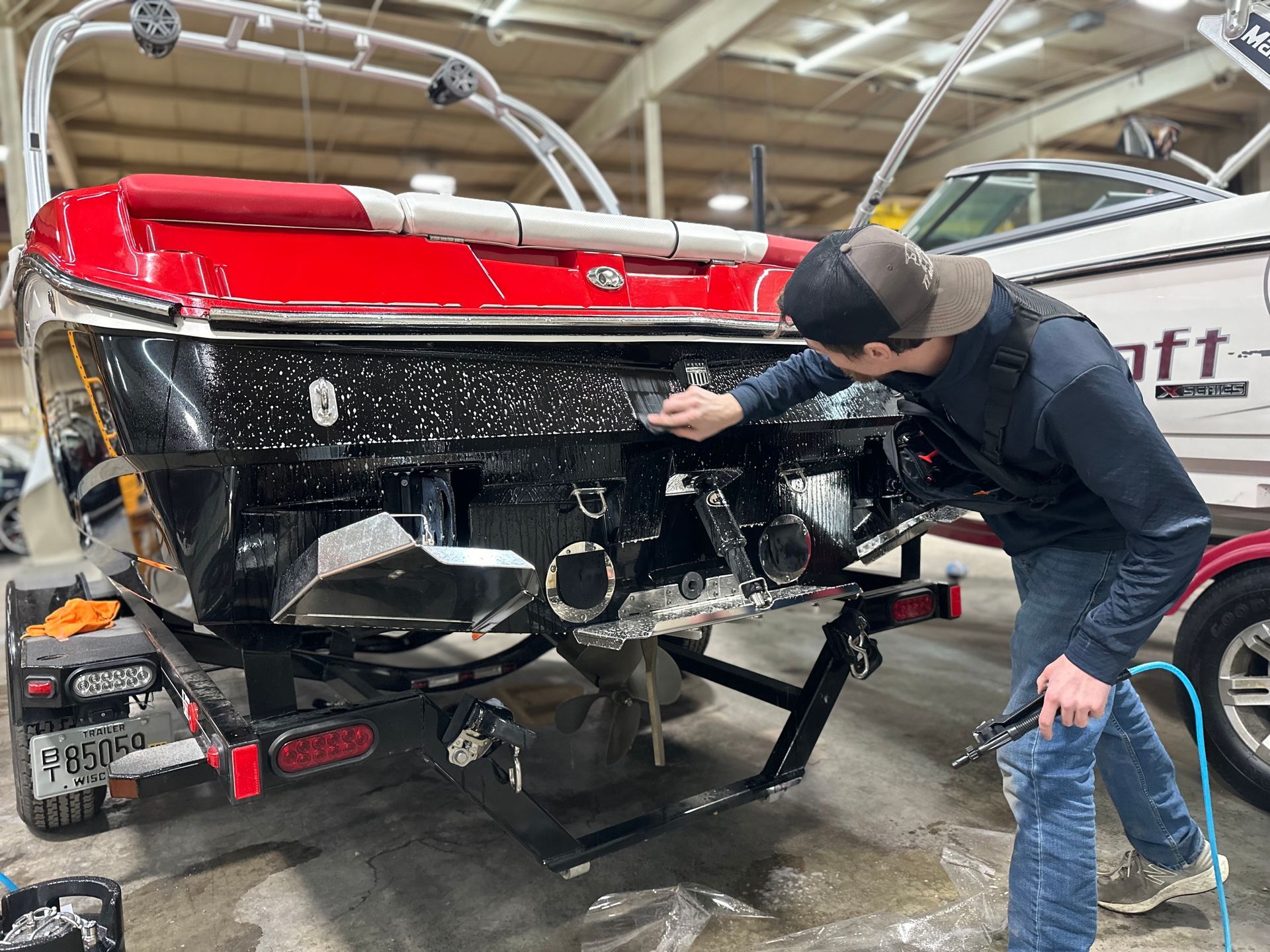 Man cleaning black boat with red accents in an indoor facility. Boat is on trailer.