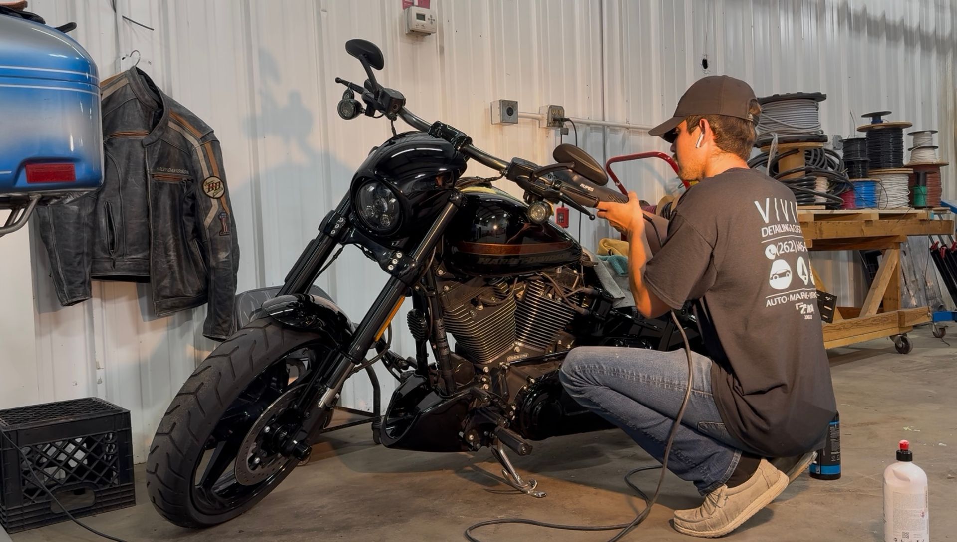 Man working on a black motorcycle in a workshop. He is focused, wearing a hat and jeans.