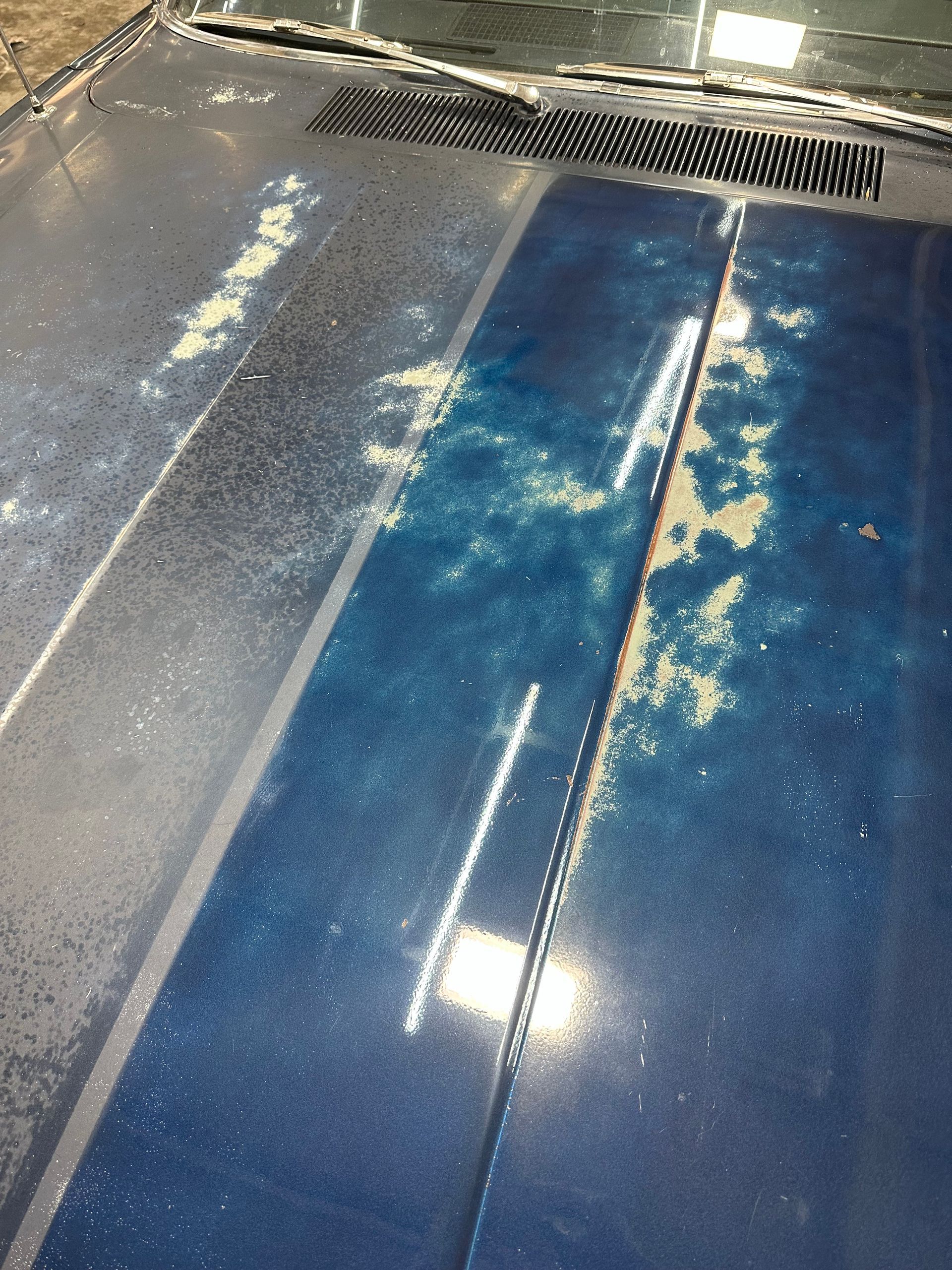 Blue car hood with peeling paint, streaks of white, and a black vent.