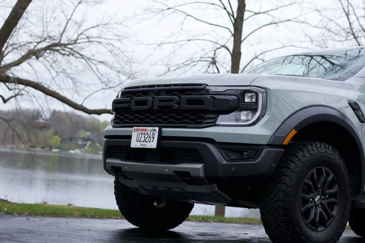 Gray Ford Raptor truck parked by a lake with a cloudy sky.