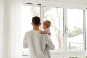 A man is holding a baby and looking out of a window.