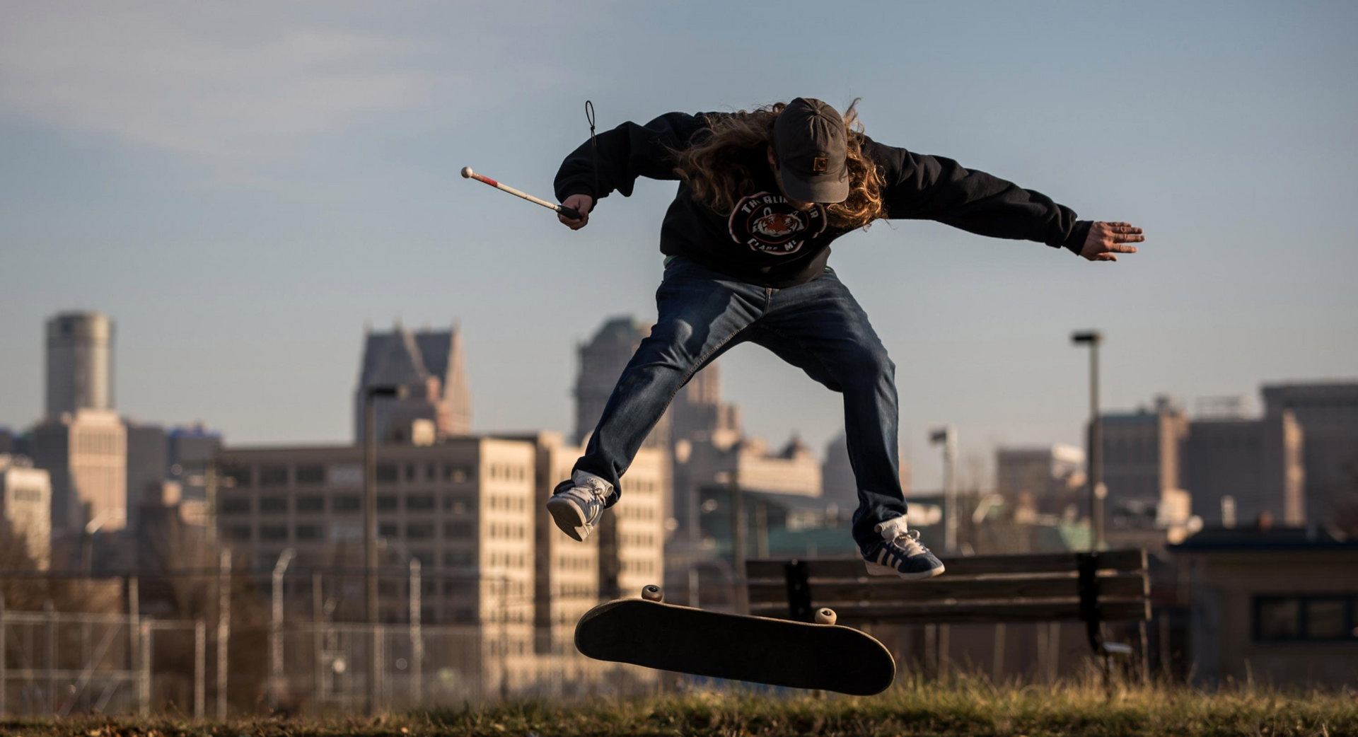 Dan does a big flip trick, cityscape in background.