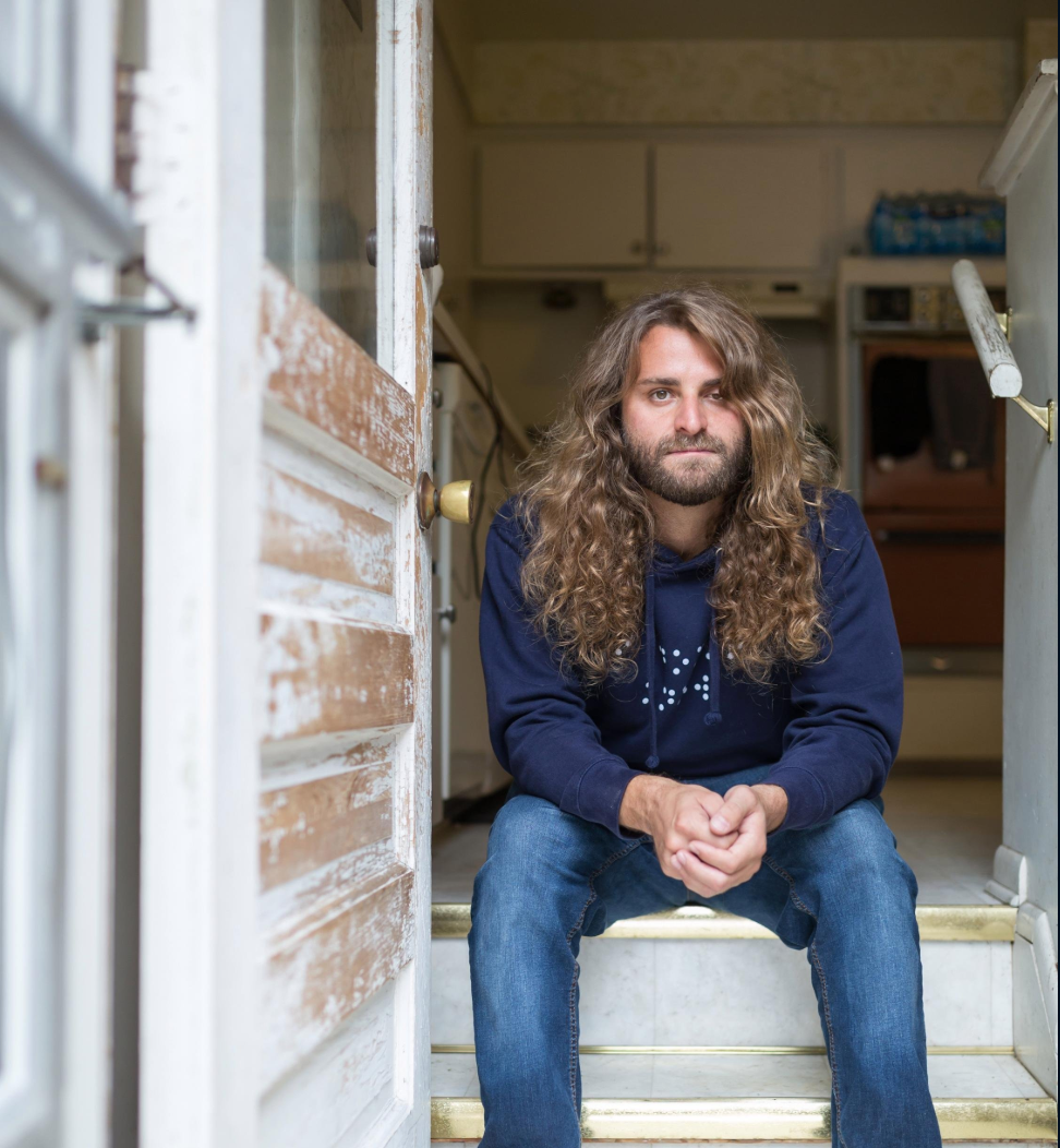 Dan Mancina sits on a stair set and faces the camera.