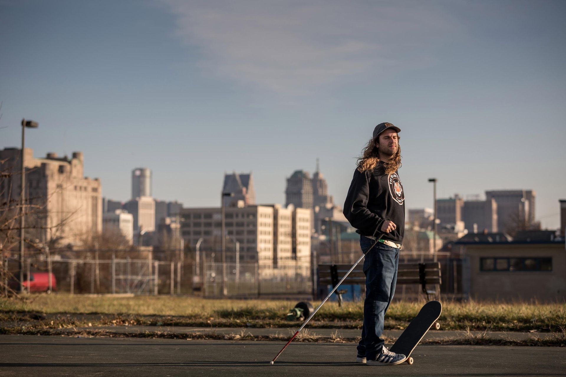 Dan poses for the camera with skateboard under foot and cane in hand.