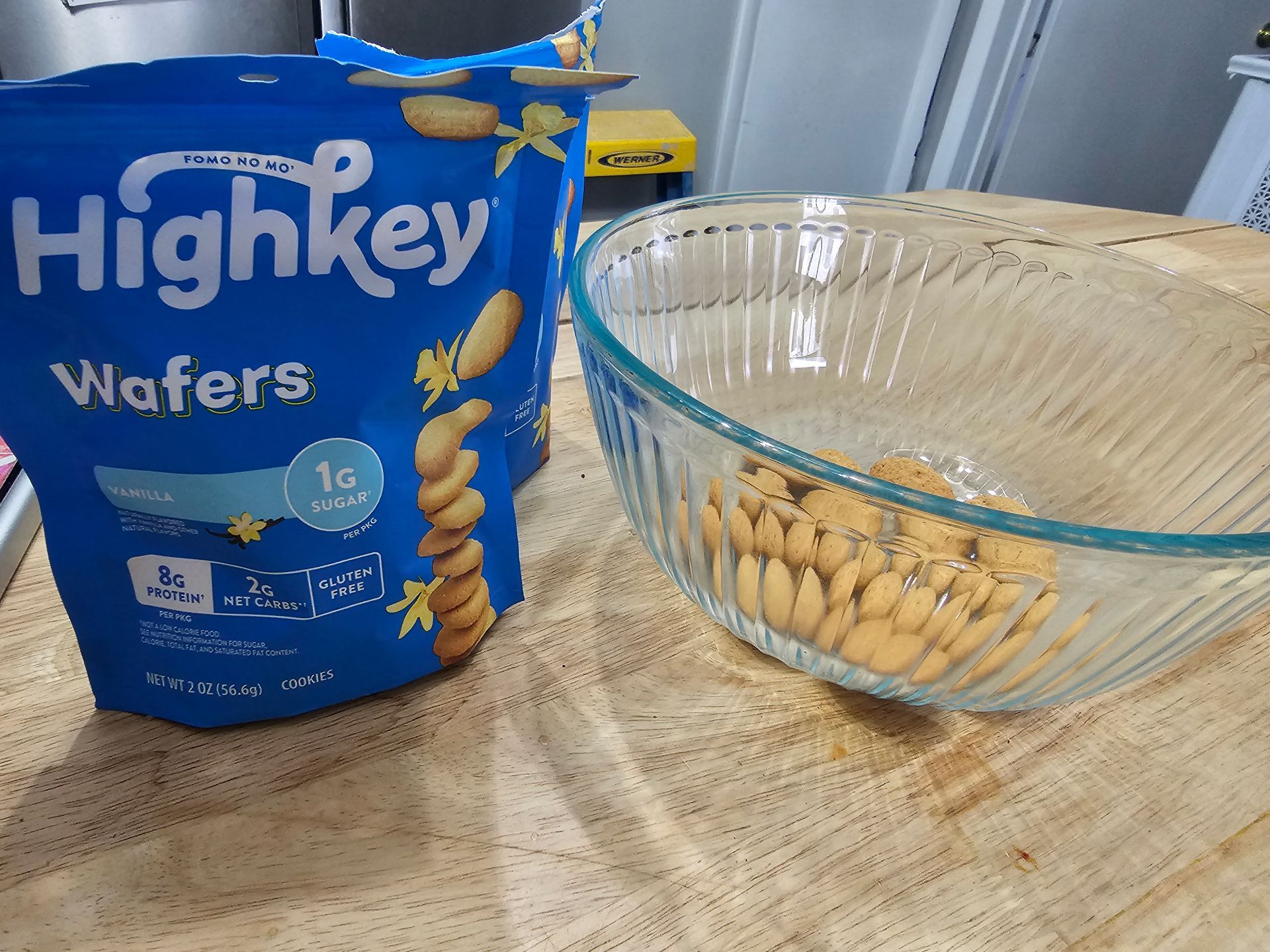 Blue bags of Highkey wafers next to a clear glass bowl with wafers inside, on a wooden surface.