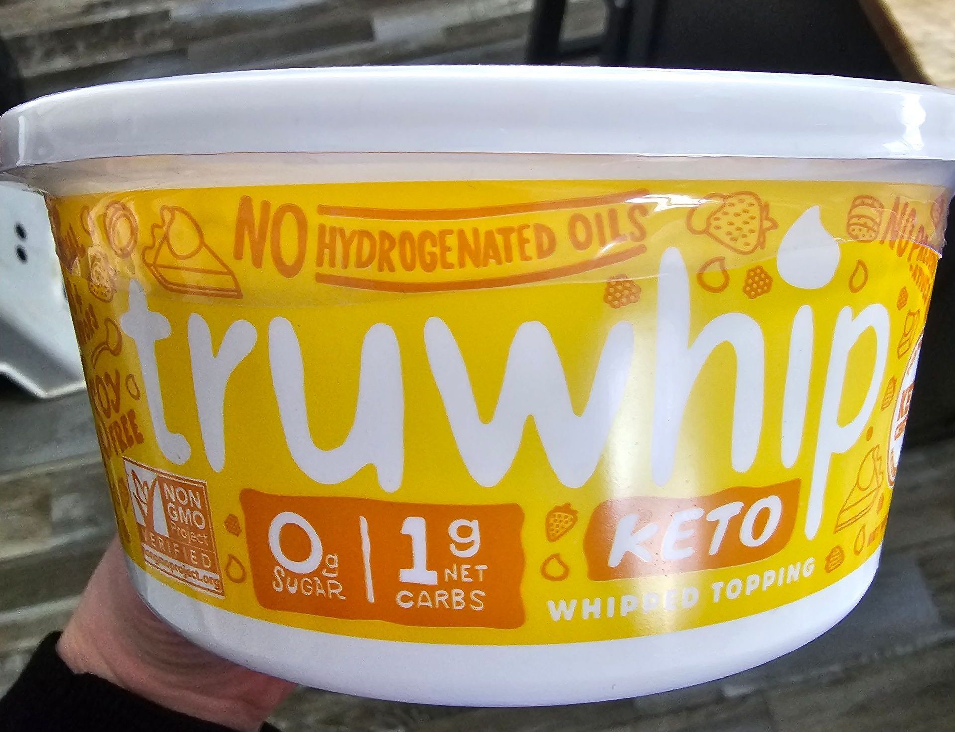 Container of Truwhip keto whipped topping, yellow label with white text, held by a hand.