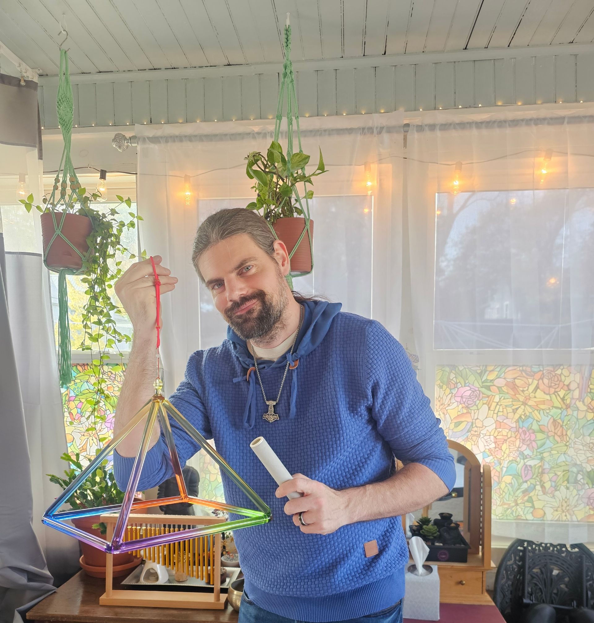 Man holding a pyramid structure, smiling, indoors with plants, and a dresser.