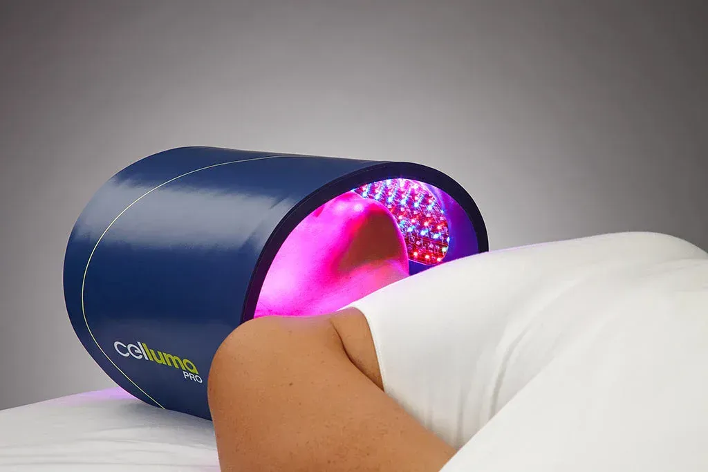 Person receiving red light therapy on their face inside a large, blue device.