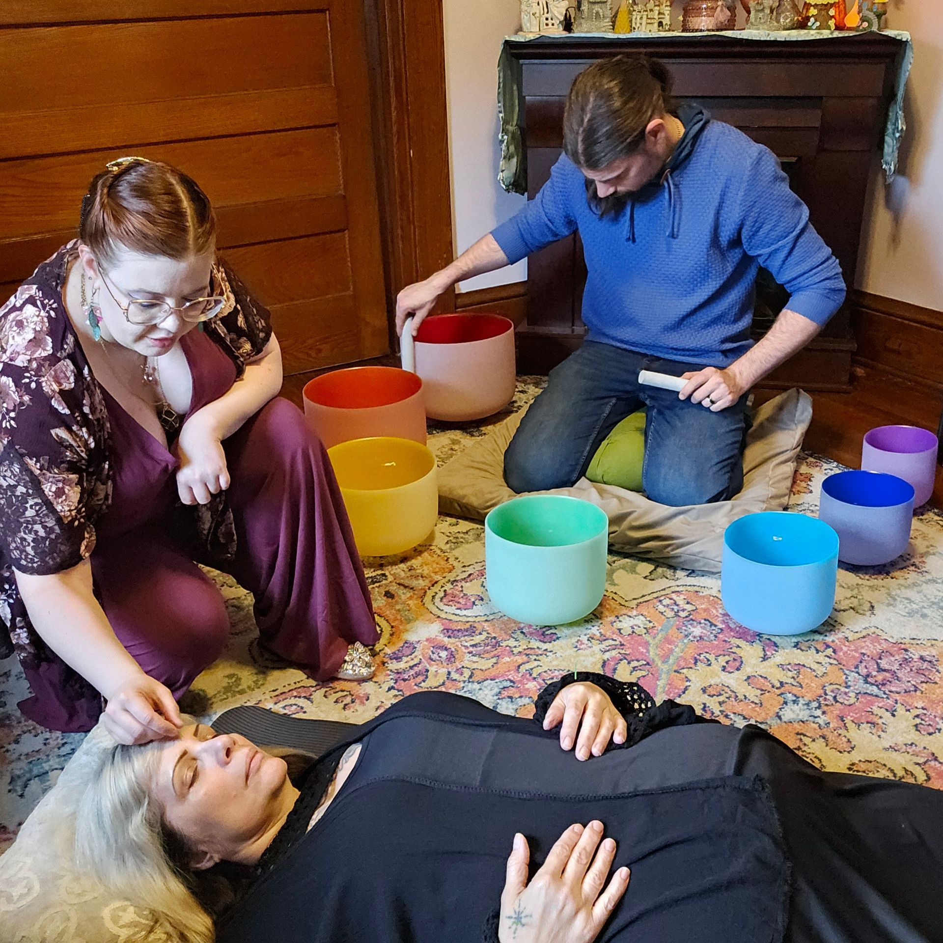 People with crystal singing bowls conducting sound healing on a woman lying down on a rug.