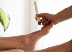Person's foot being treated with a burning moxa stick. Light setting, hands visible.