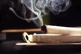 Lit moxa stick releasing smoke, held over a support, against a dark background.