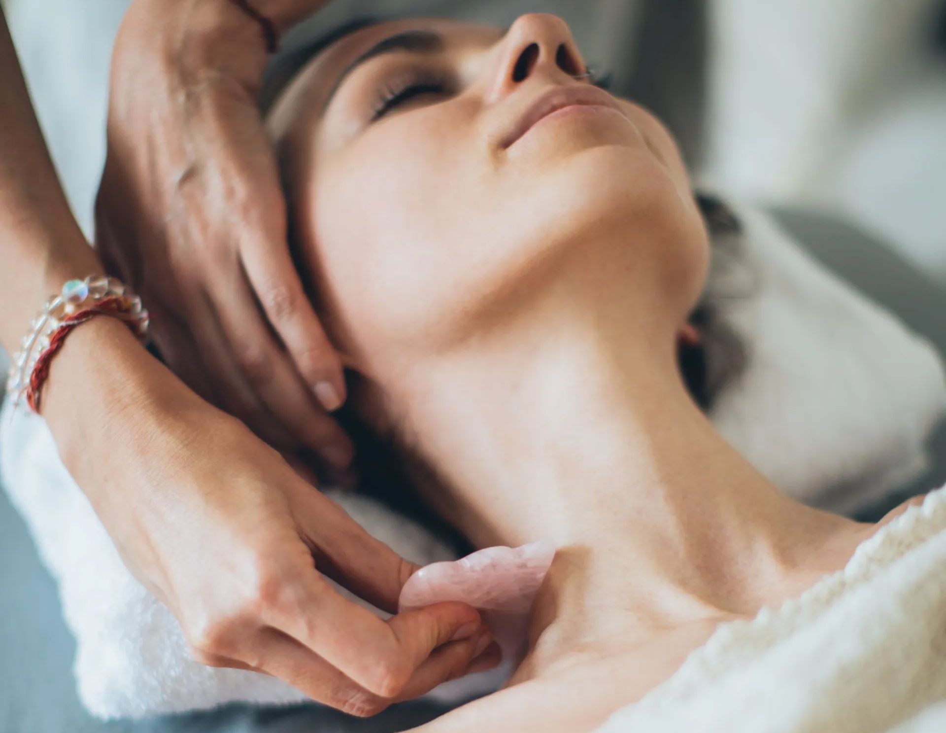 Woman receiving facial treatment with a rose quartz stone, lying on a towel.