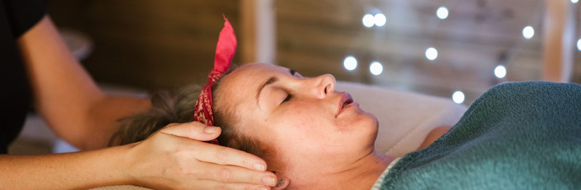 Woman receiving reiki. She is relaxed with a red bandana, the masseuse's hands on her face.
