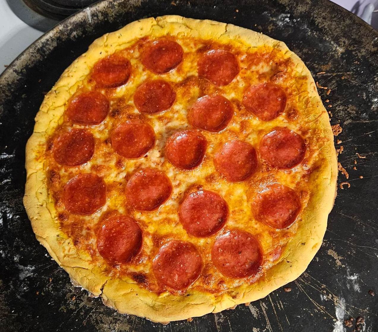 Pepperoni pizza on a dark baking sheet.