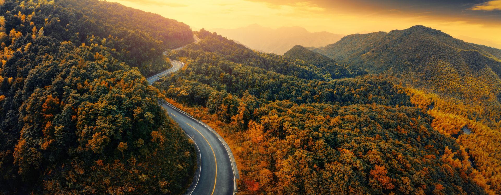 A winding road through a lush, green mountain range, bathed in golden sunlight.