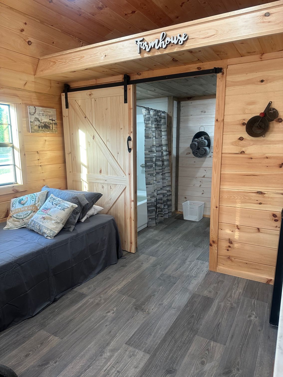 Cozy cabin interior with wood paneling, a bed with pillows, sliding barn door, and a bathroom with a stone accent wall.