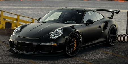 Black sports car parked on asphalt by a yellow barrier, front three-quarter view | Kars Performance