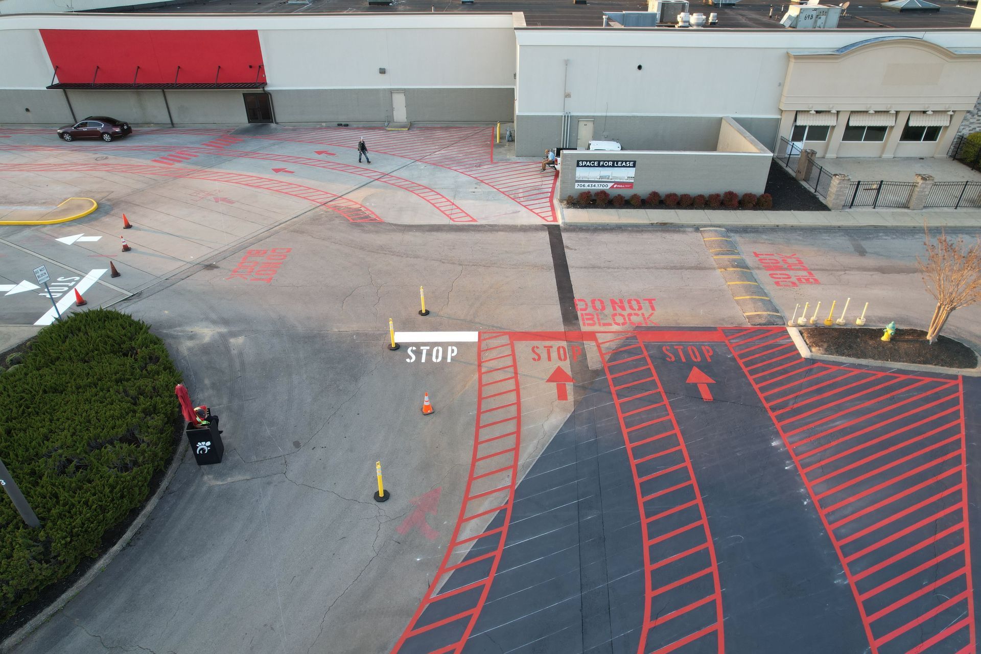 Aerial view of an empty parking lot with red-striped no-parking zones and traffic markings near a loading dock.
