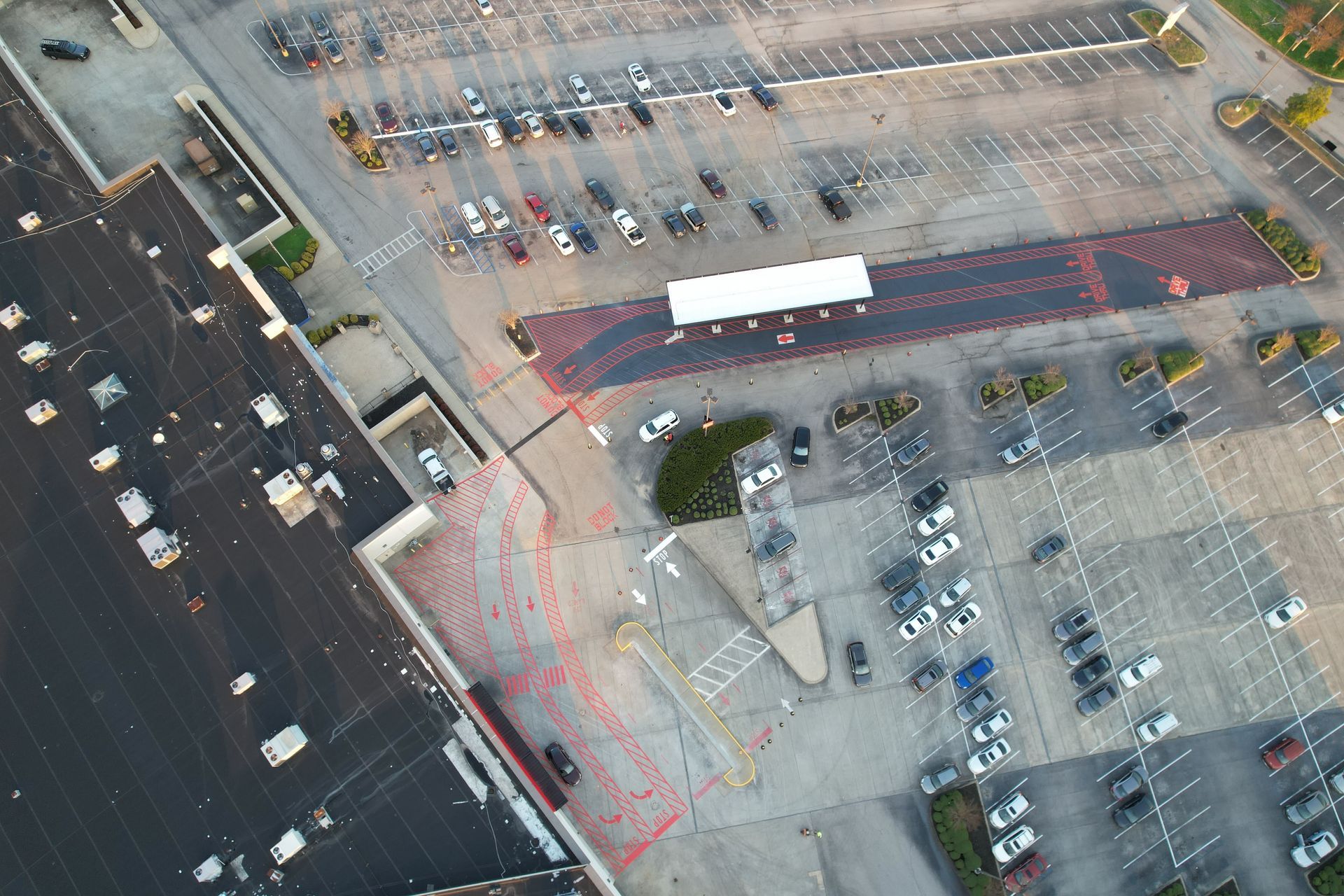 Aerial view of a parking lot beside a large building with marked lanes and parked cars.