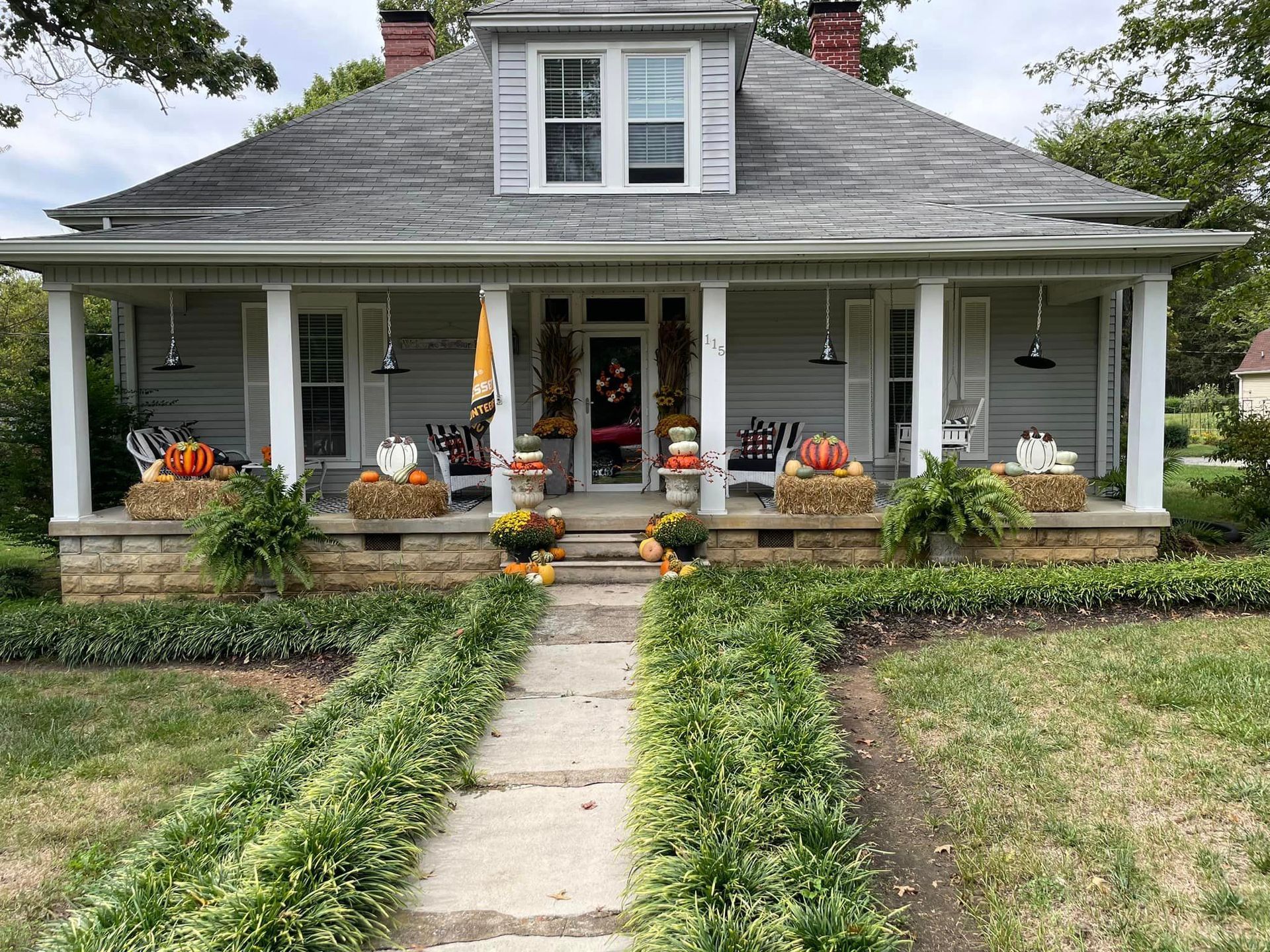 A house with a porch decorated for fall with pumpkins and flowers.