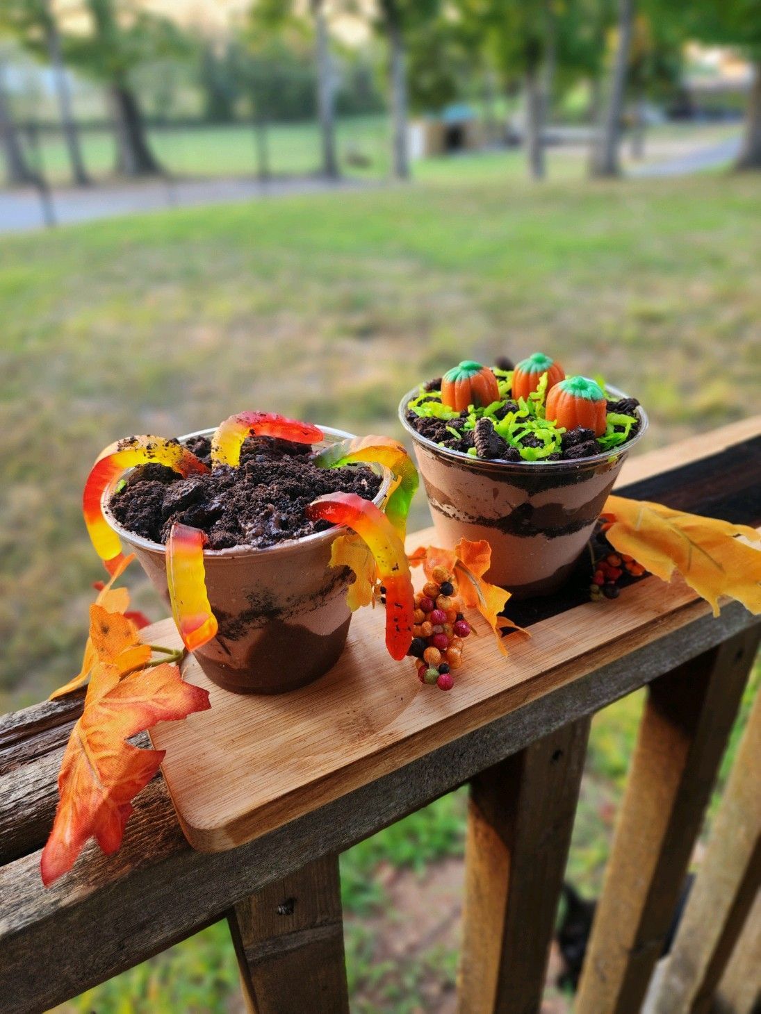 Two cups of dessert are sitting on a wooden railing.