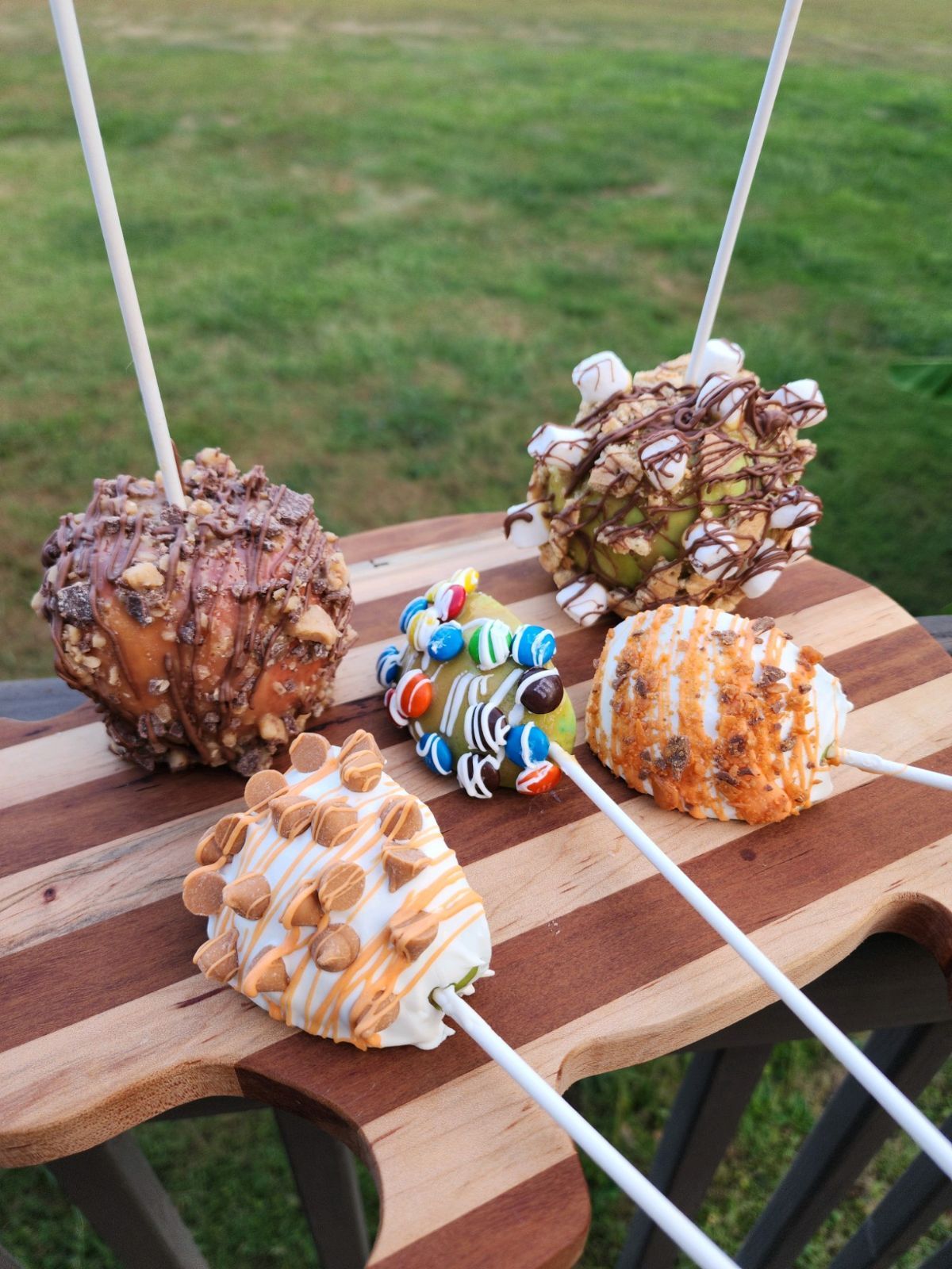 A wooden cutting board with four different types of marshmallows on sticks.