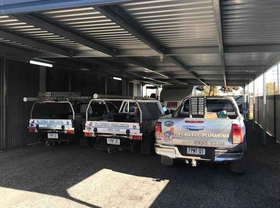 A Row Of Trucks Parked Under A Canopy In A Parking Lot — Flavell Plumbing (NT) Pty Ltd In Ciccone, NT