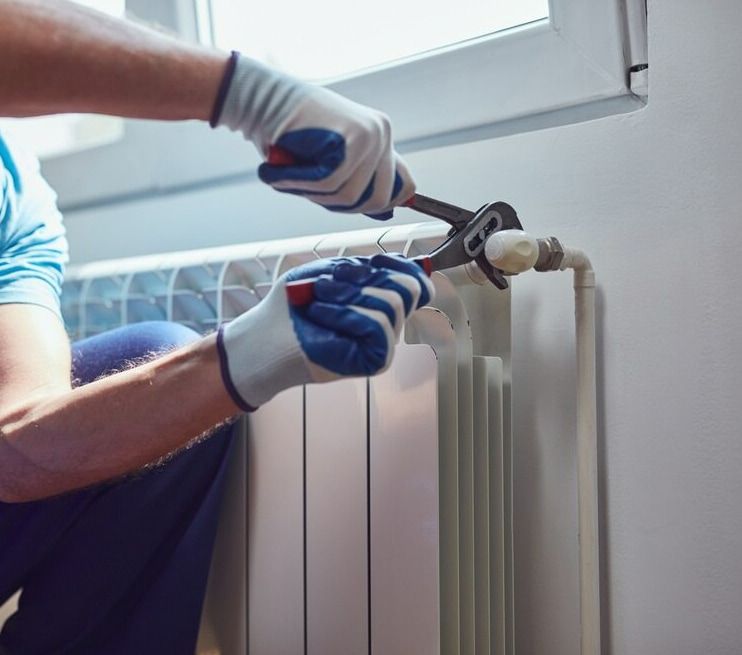 A Man Is Fixing A Radiator With A Wrench — Flavell Plumbing (NT) Pty Ltd In Ciccone, NT