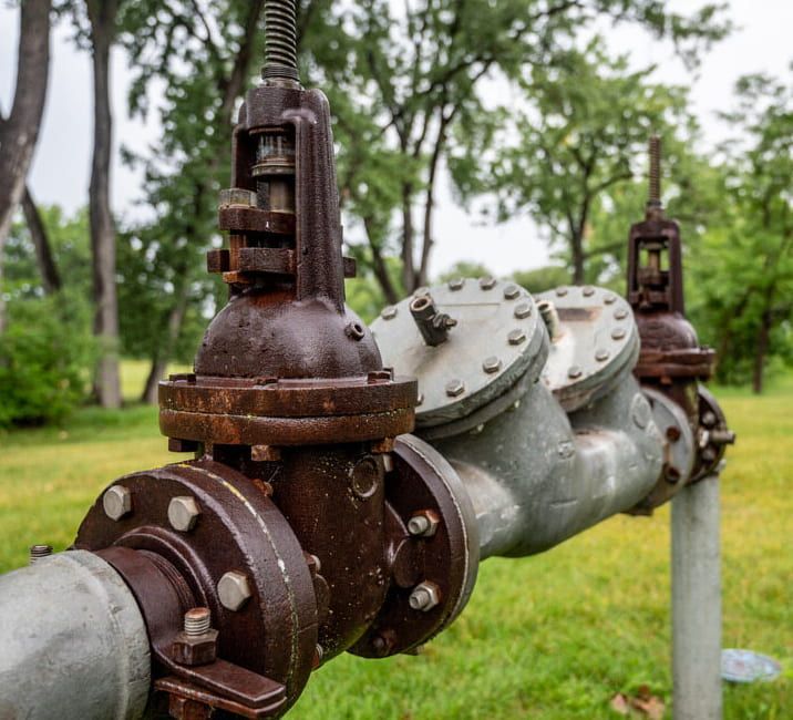 A Row Of Rusty Valves On A Pipe In A Field — Flavell Plumbing (NT) Pty Ltd In Ciccone, NT