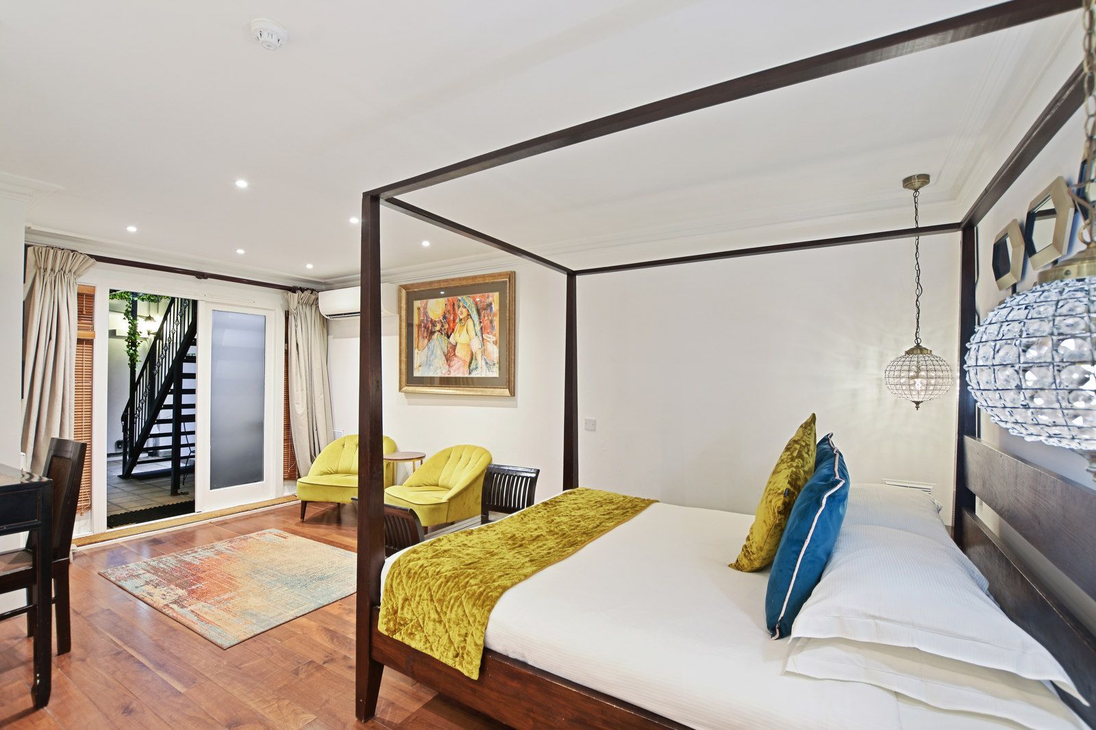 Bedroom with four-poster bed, yellow accents, and glass doors opening to stairs.