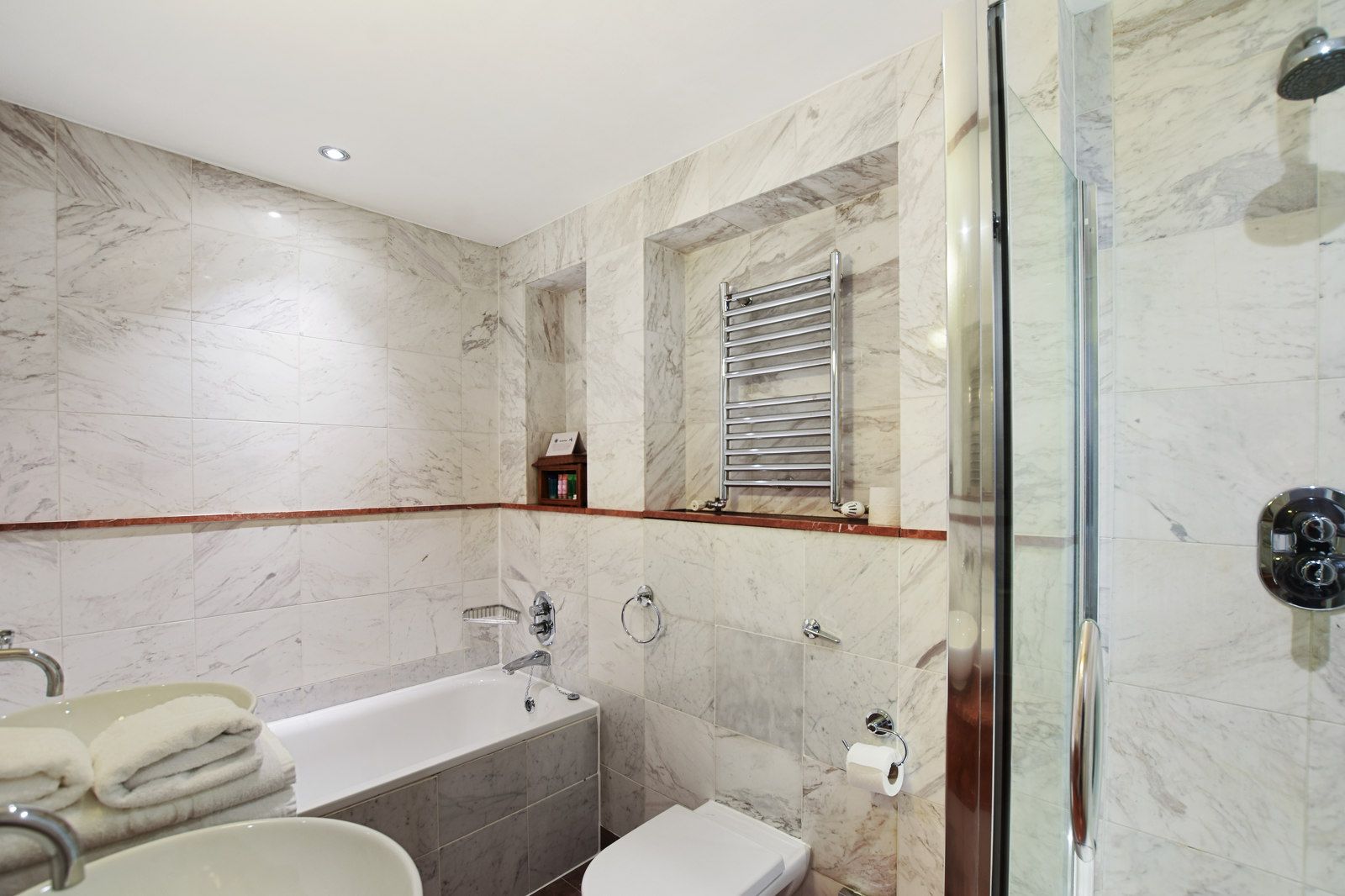 Bathroom with marble walls, a tub, toilet, and shower. Towels on the counter.
