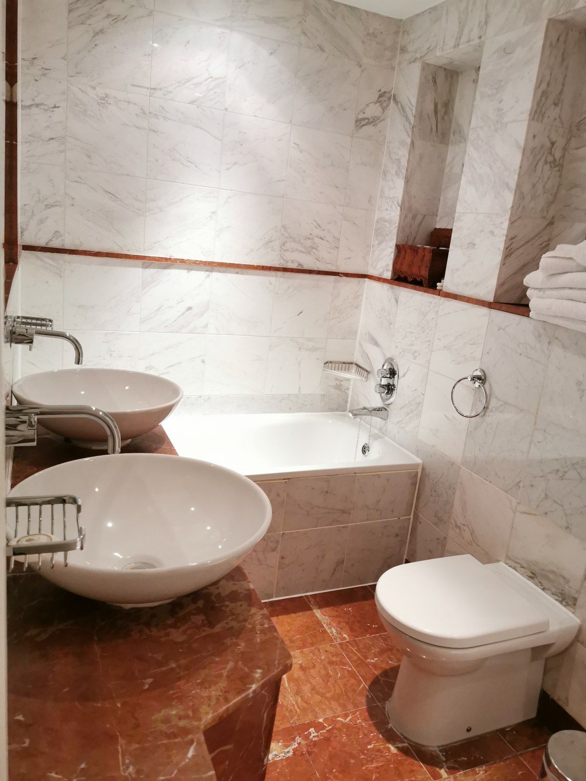 Marble bathroom with dual sinks, bathtub, and toilet. Light-colored walls and countertops.