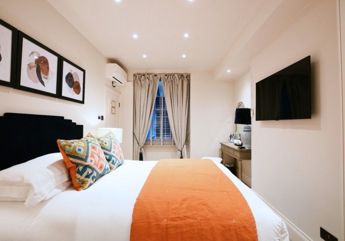 Bedroom with bed, pillows, TV, window with curtains, and artwork.