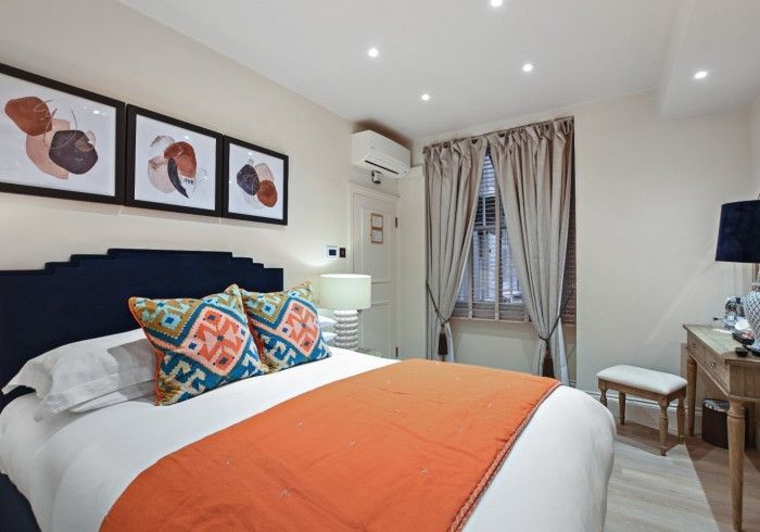 Bedroom with a bed, artwork, a window, and a desk. Orange and blue accents, neutral walls.