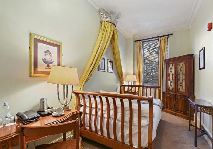 Hotel room with bed, wooden furniture, artwork, and yellow canopy.