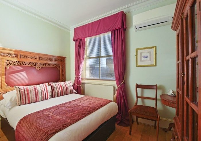 Bedroom with wooden bed, red bedding and curtains, chair, wooden cabinet, and light green walls.