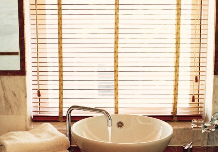 Bathroom sink with running water, in front of closed wooden blinds, marble wall, and a towel.