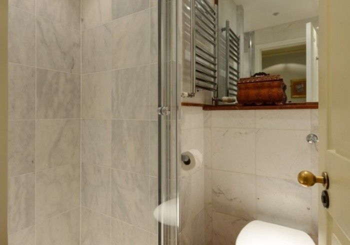 Small bathroom with a marble-tiled wall, glass shower door, and a toilet. There is a towel rack.