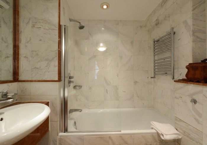 Bathroom with white marble tile, bathtub, glass shower door, sink, and heated towel rack.