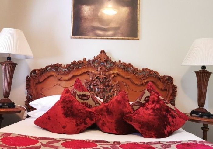 Bedroom with ornate wooden headboard, red velvet pillows, two lamps, and a Buddha image above the bed.