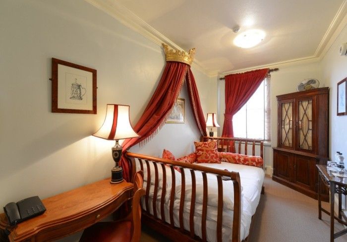 Bedroom with crown canopy bed, red curtains, wooden desk, and cabinet.