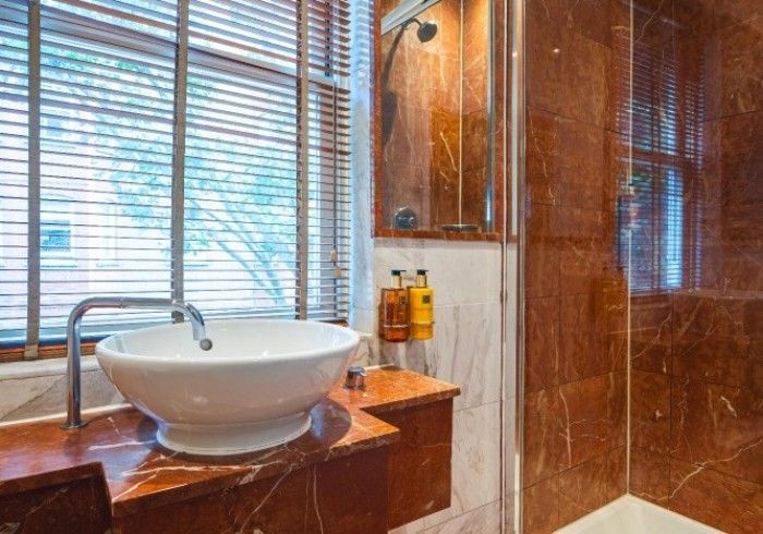Bathroom with a round sink, brown marble walls, a window with blinds, and a shower.
