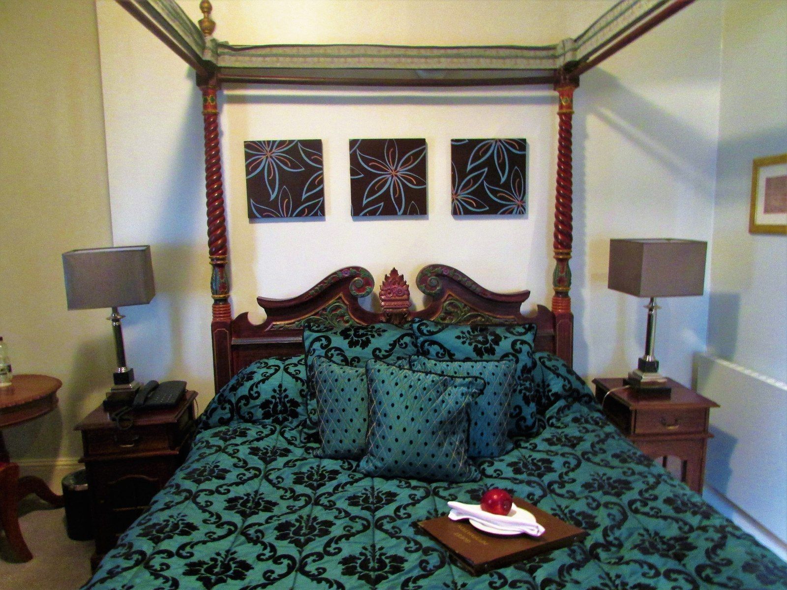 Bedroom with canopy bed, teal and black bedding, nightstands, and artwork on wall.