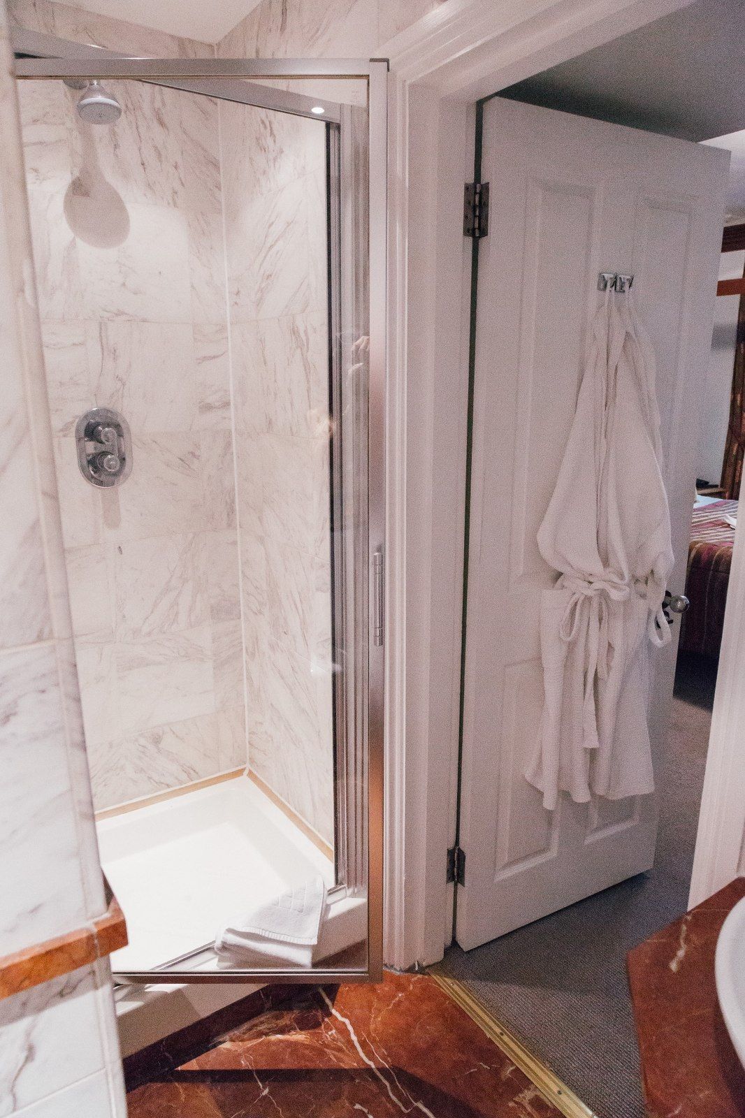 Shower stall with marble walls, open door with robe, and adjacent sink.
