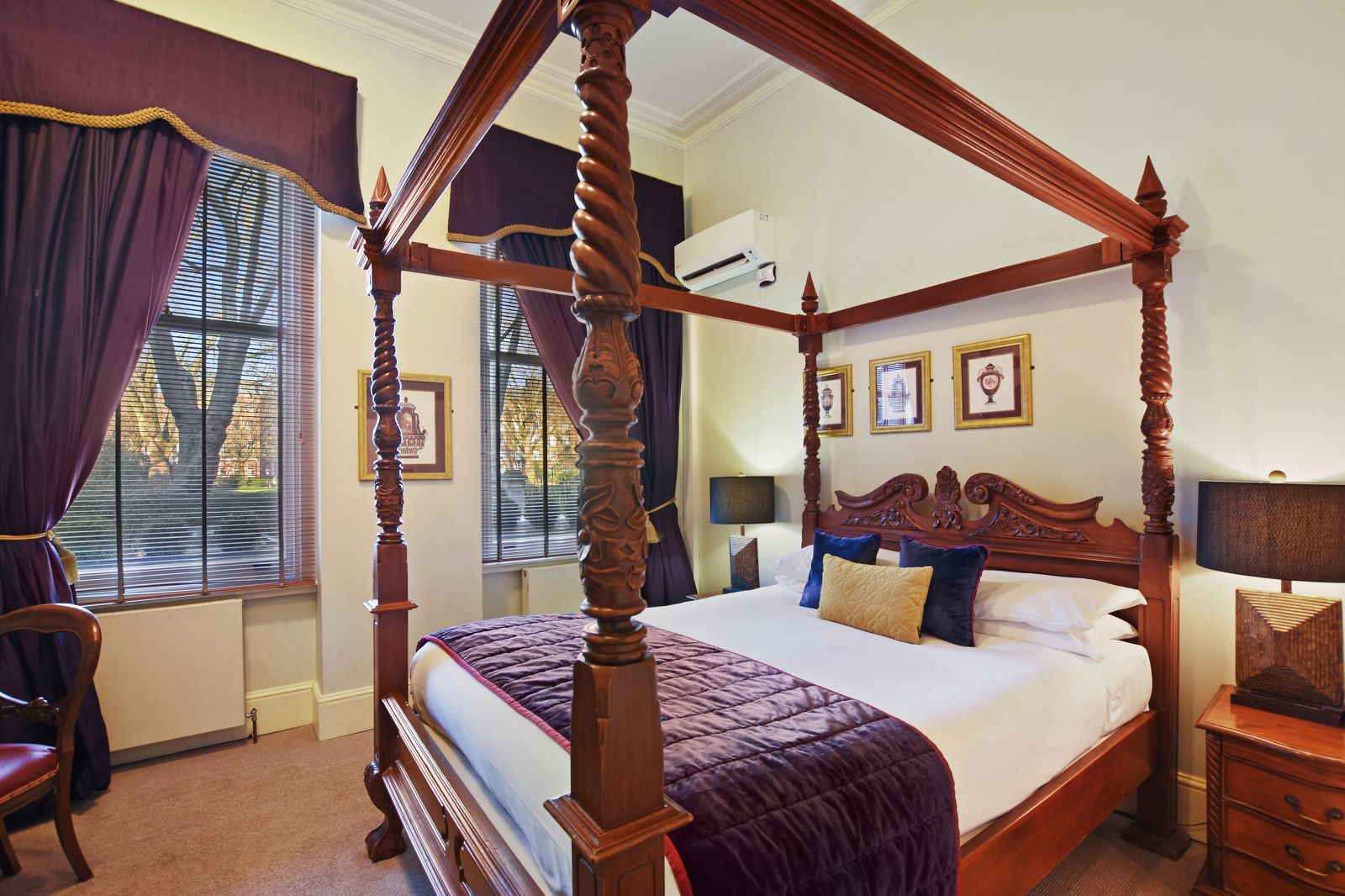Bedroom with four-poster bed, purple drapes, and ornate details; lamp and nightstand on the right.