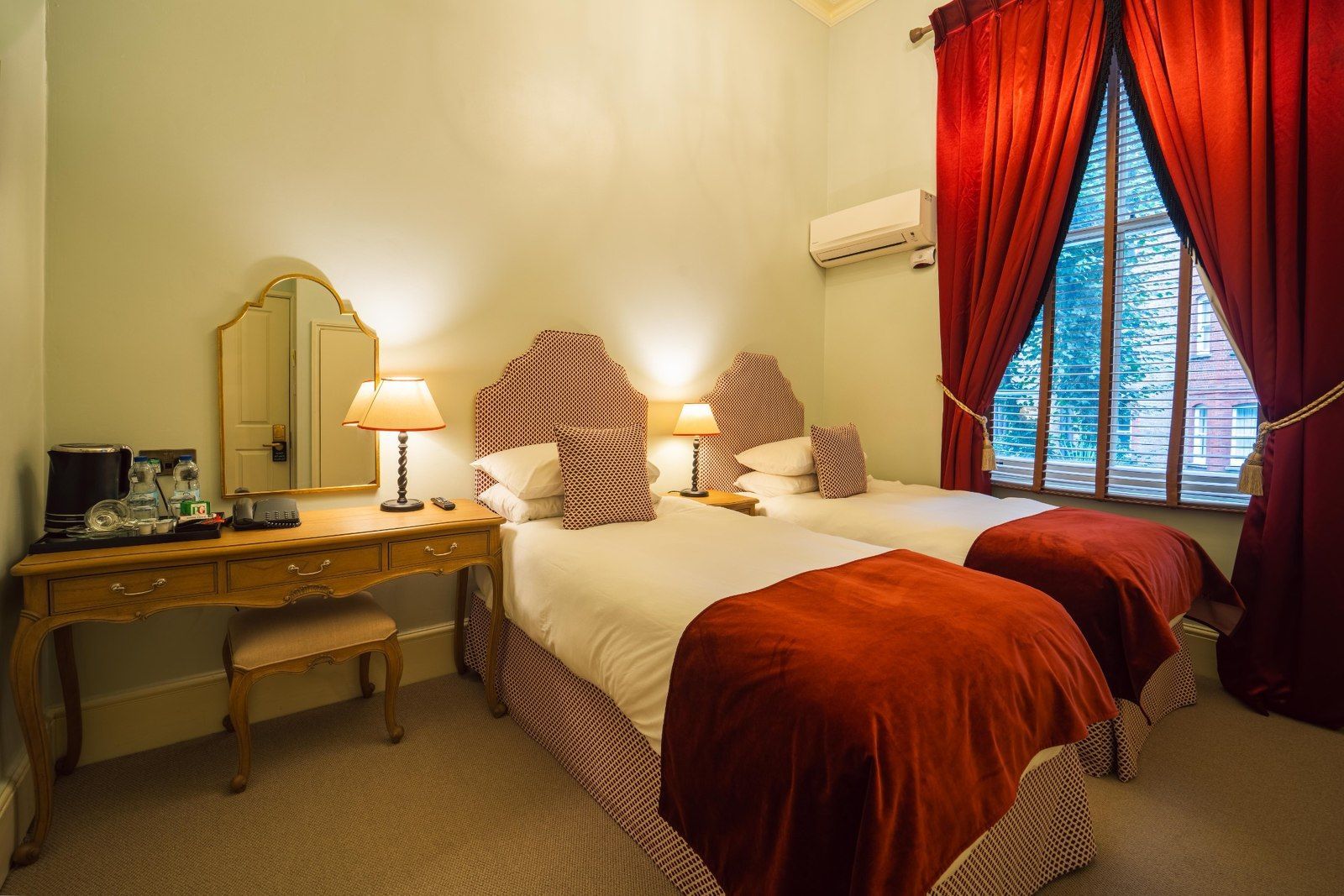 Bedroom with two twin beds, desk, red curtains, and decorative headboards.
